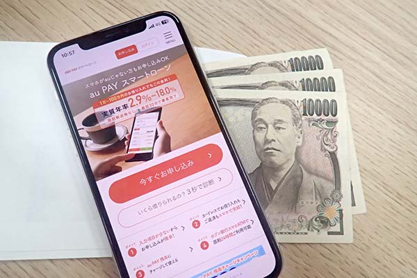 au PAY スマートローンの公式ホームページを表示させたスマホ画面とお金